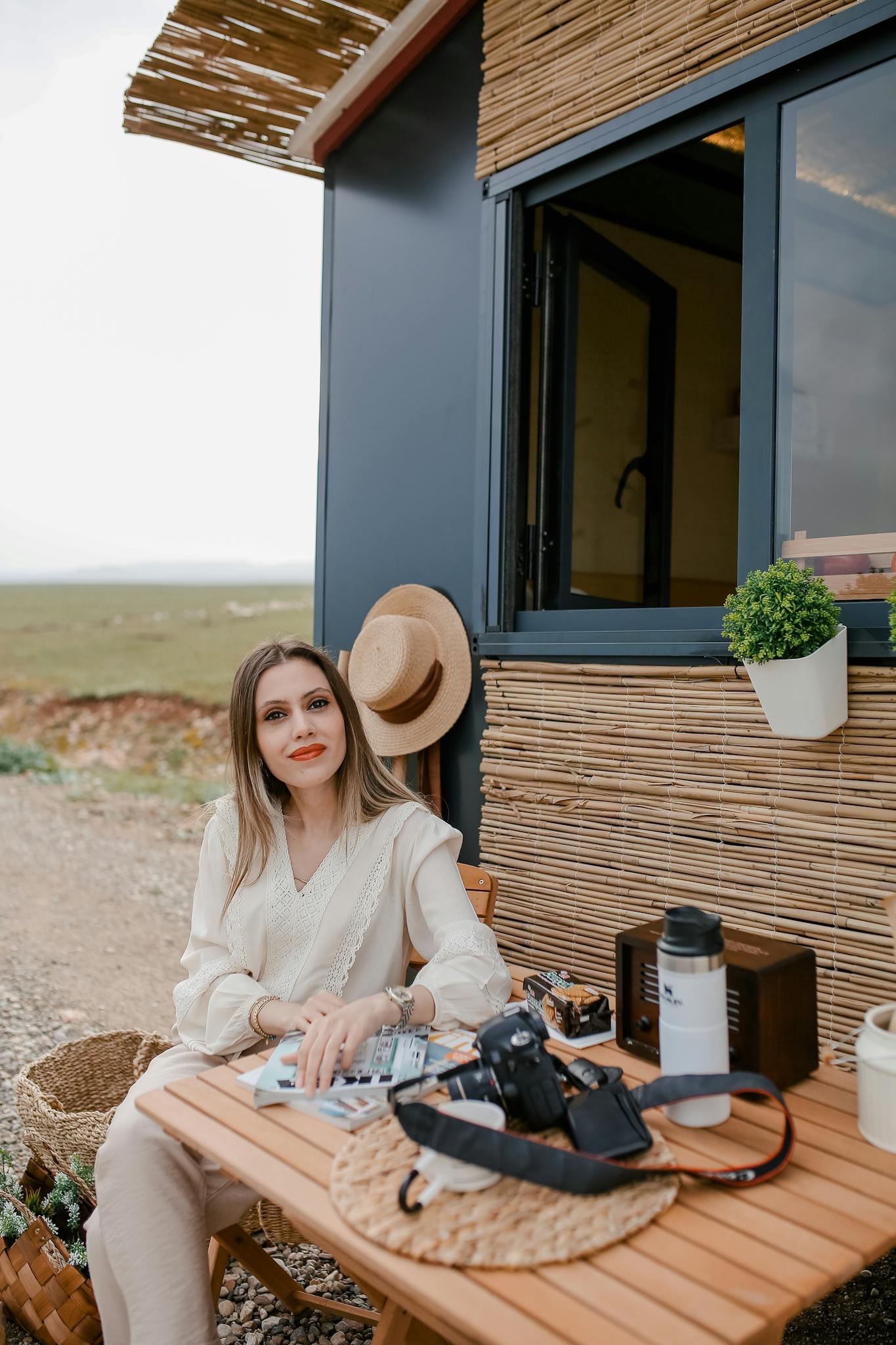 Woman sitting outside a tiny house on a road trip, capturing moments with a camera.